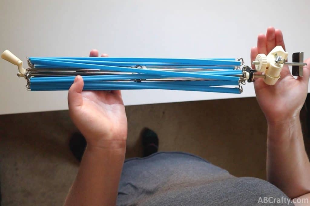 holding a blue plastic yarn swift above a white table