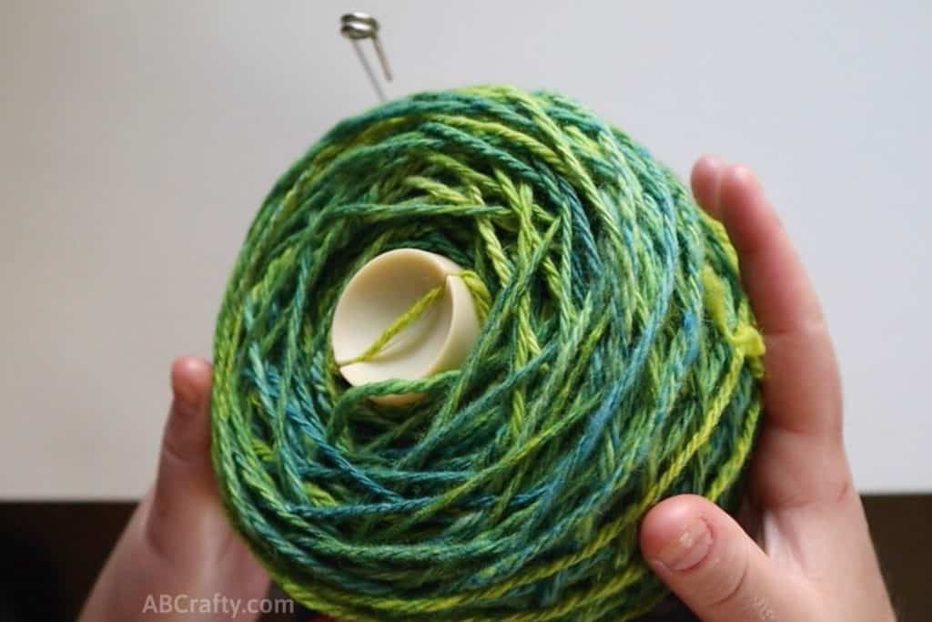 holding a cake of green yarn and pulling it off of a winder