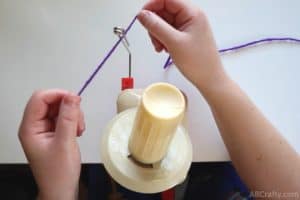 passing purple yarn through the metal feed of a yarn winder