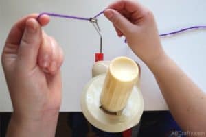 lifting purple yarn up through the loops of the feeder