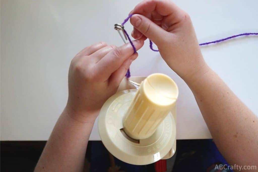 pulling purple yarn through the last loop of the metal feeder