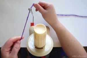 purple yarn fed through the metal part of a yarn ball winder