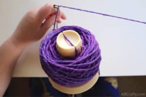 holding the metal part of a yarn ball winder with partially wound up ball of purple yarn