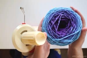 holding a ball of blue and purple yarn next to a yarn ball winder