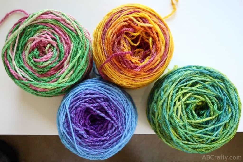 four cakes of yarn in green, yellow, blue, and pink and green