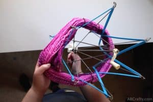 placing a hank of pink yarn onto a blue plastic yarn swift while pulling on the handle to expand the yarn swift