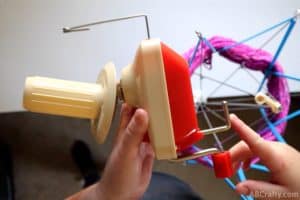 pointing to the bottom part of a yarn winder with a yarn swift in the background