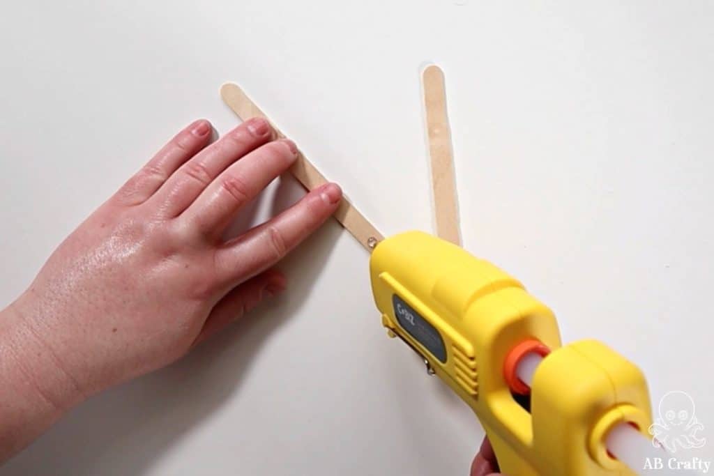 using a yellow glue gun to add glue to the end of a popsicle stick