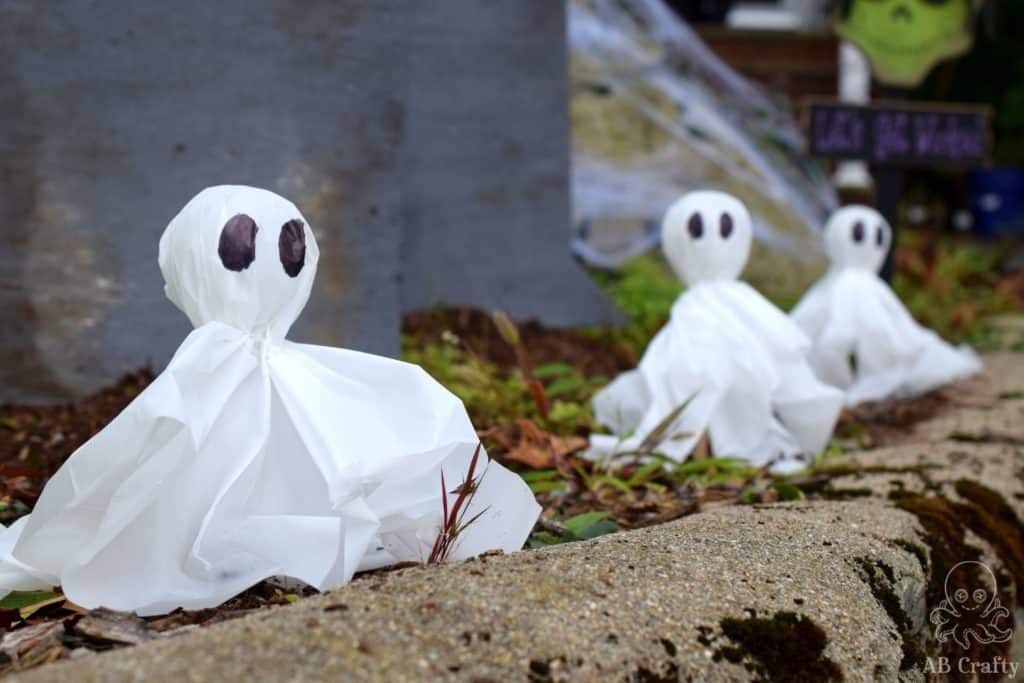 DIY outdoor halloween lights in the shape of ghosts lining the pathway with homemade gravestones behind them
