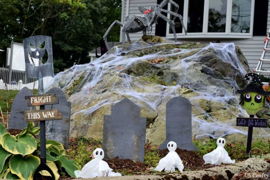 halloween lights and decorations on the front line with the diy ghost lights lining the path, homemade gravestones, and an animatronic spider on top of a large rock