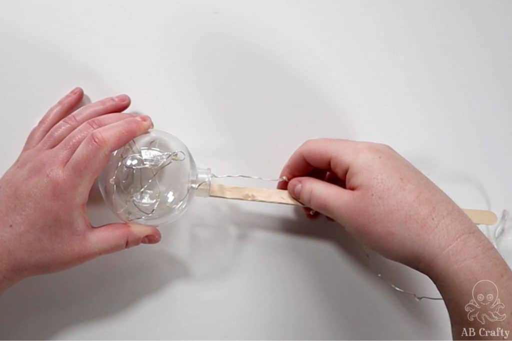 pressing a popsicle stick to a plastic fillable ornament