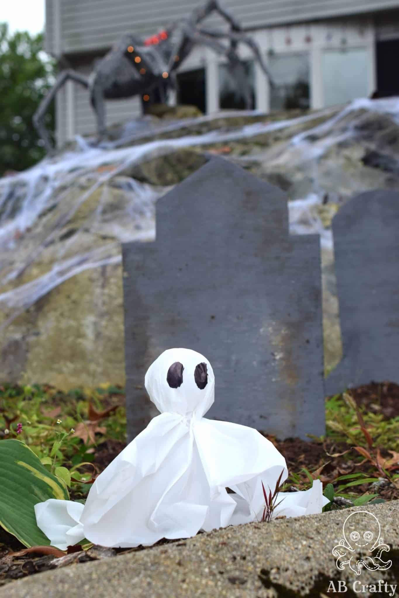 DIY ghost light in front of a diy gravestone in front of an animatronic spider on top of a large rock in front of a house