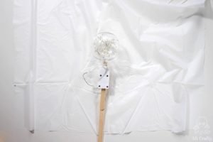 a clear plastic ornament filled with fairy lights and glued to a popsicle stick on top of a piece of white plastic tablecloth