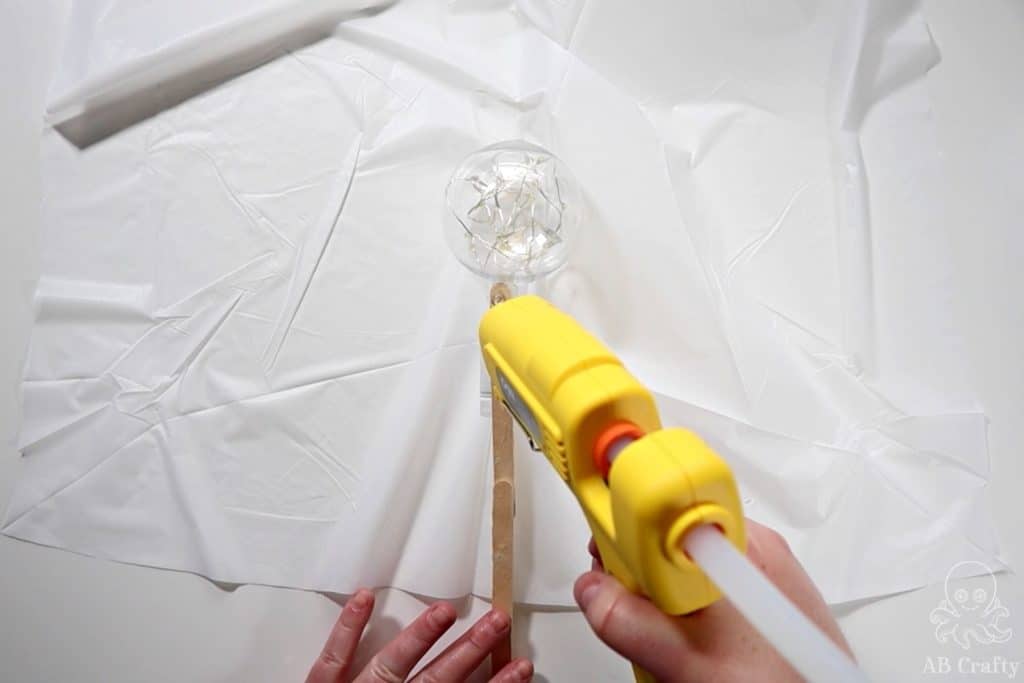 adding glue to the base of a plastic ornament on top of a white plastic tablecloth