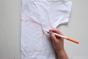 using an orange washable marker to draw the outline of a pumpkin on a folded white shirt