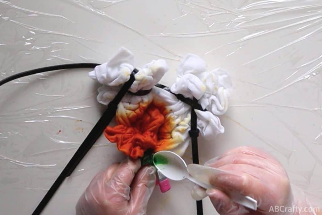 pouring green dye onto a tied up shirt to form the tie dye pumpkin