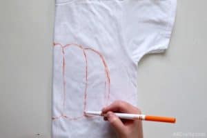 using an orange washable marker to draw the inside lines of a pumpkin on a folded white shirt