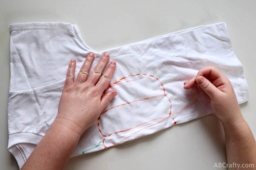 the outline of an pumpkin sewn with orange thread on a folded shirt