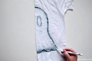 drawing the outline of a ghost tie dye design with a washable marker on a folded white shirt