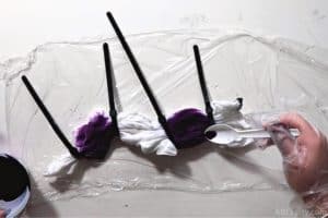 pouring dark purple dye from a spoon onto a section of the tied white shirt