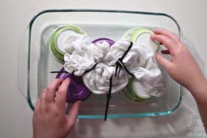 Placing a tied up white shirt on top of yogurt containers in a glass 9x13 pan