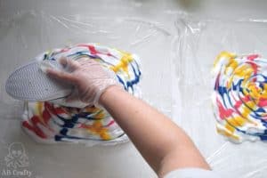 placing a white converse shoe face down onto shaving cream with swirled with tie dye