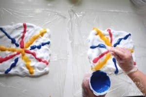 pouring blue tie dye mixed with shaving cream onto shaving cream with tie dye on it