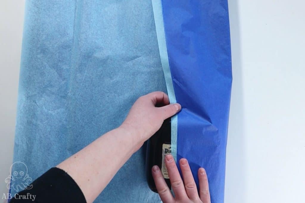 folding over the two blue pieces of tissue paper around the bottle