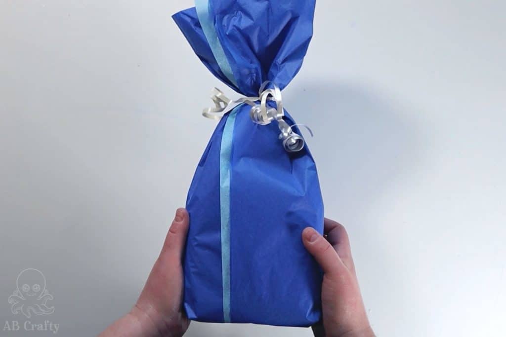 holding the finished present wrapped in blue tissue paper with silver curled ribbon