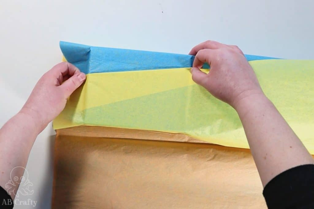 folding the yellow tissue paper at an angle on the top of the gift box