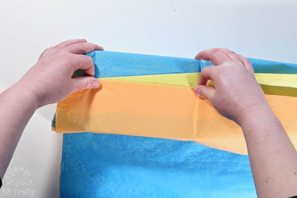 folding the orange tissue paper in a straight line to form a triangle of the yellow paper