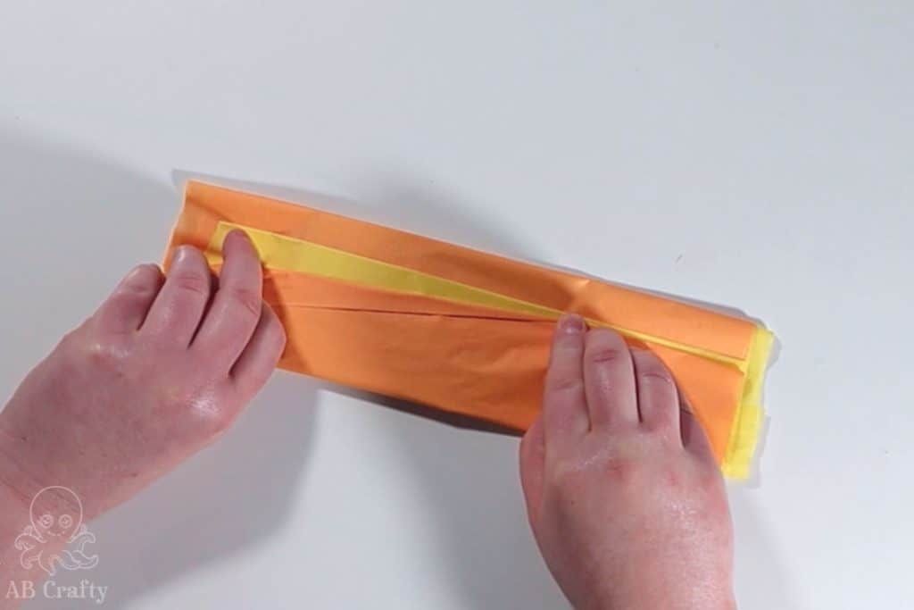 folding orange tissue paper backwards to form a triangle and reveal a yellow stripe