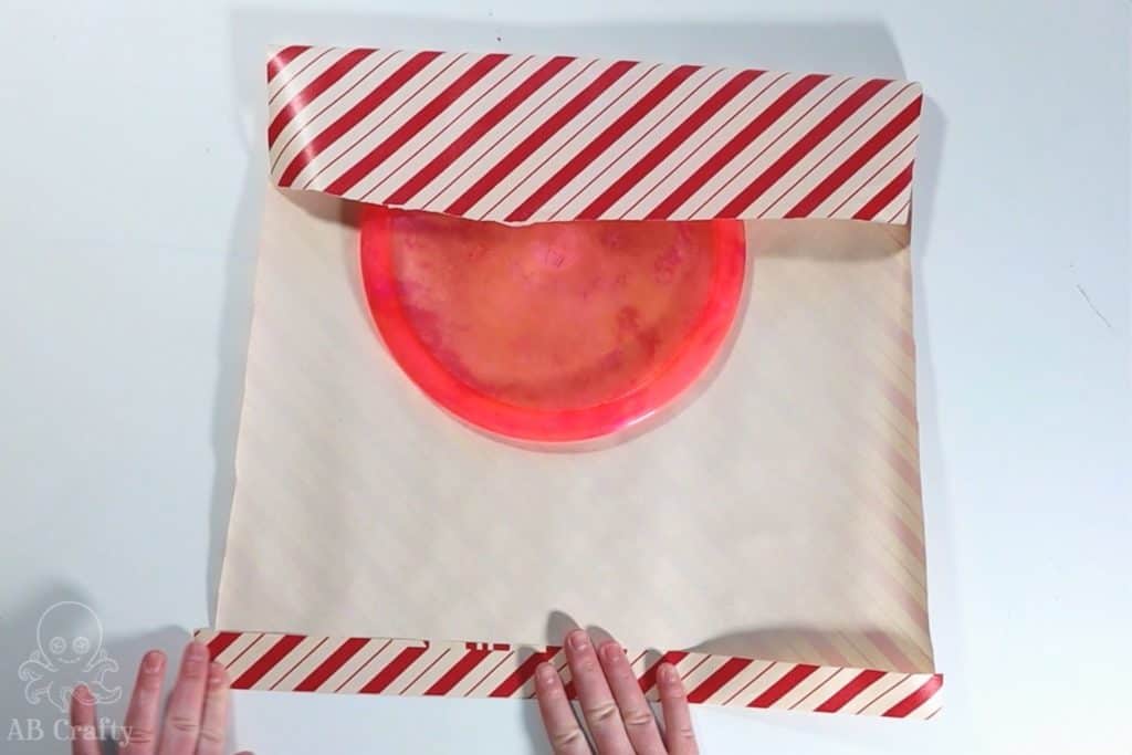 folding over the edge of the wrapping paper to wrap a dyed frisbee golf disc