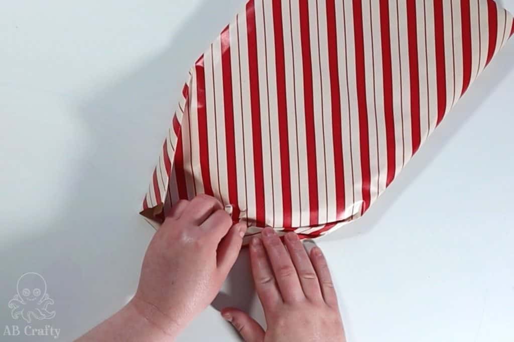 folding the edge of red and white striped wrapping paper around a circular object