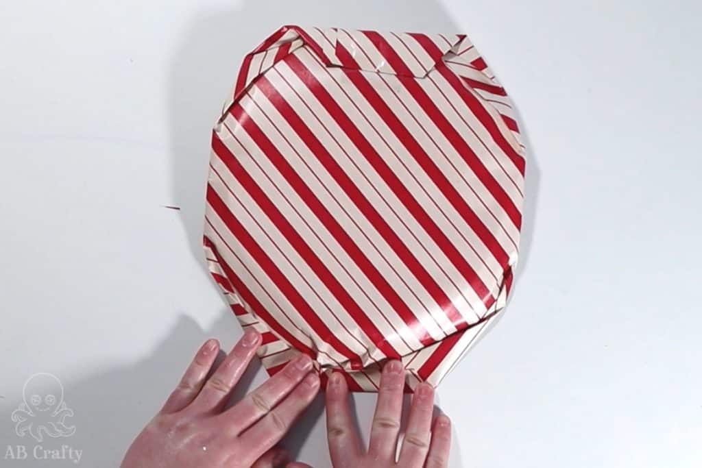 folding over the edge to form a clean line of wrapping paper around a circular object
