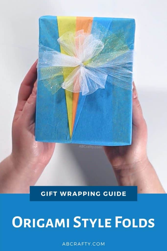 holding the finished origami style wrapped present with blue yellow and orange tissue paper forming triangles and a ribbon made of white tulle and the title reads "gift wrapping guide - origami style folds"