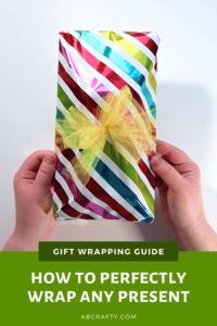 holding the finished wrapped present with rainbow wrapping paper and a tulle bow and the title reads "gift wrapping guide - how to perfectly wrap any present"