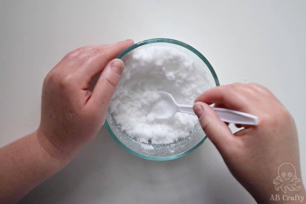 mixing instant snow in a glass bowl with a plastic spoon