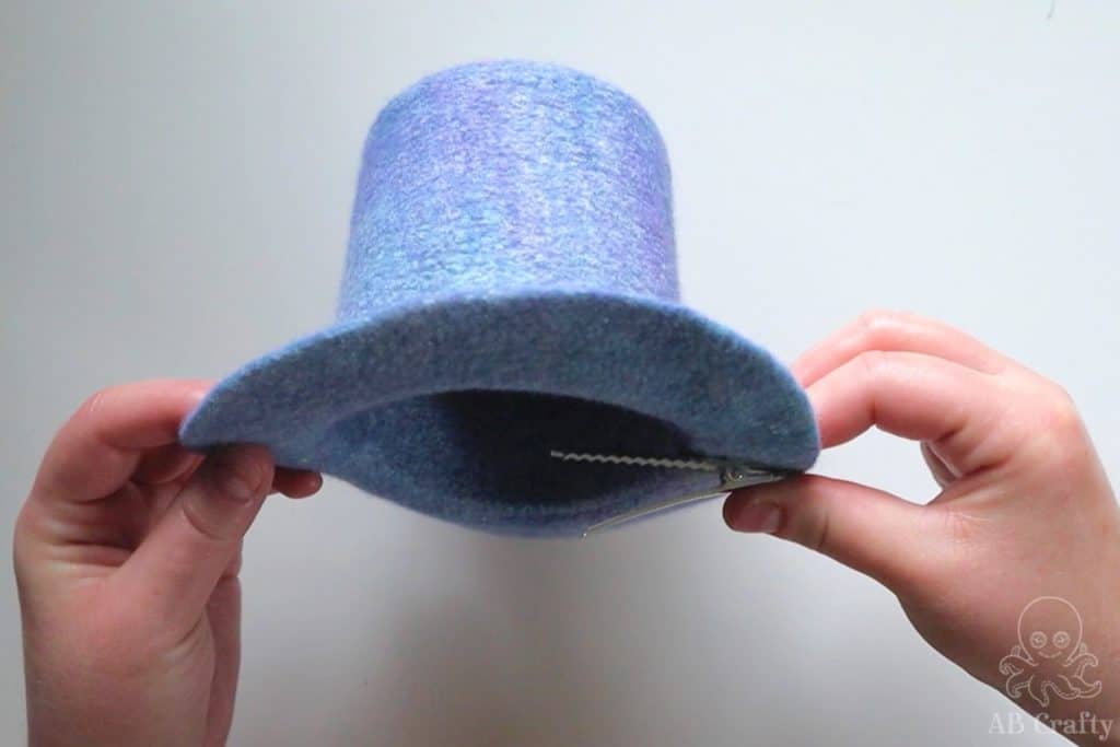 opening the alligator clip while holding the blue wet felted mini top hat