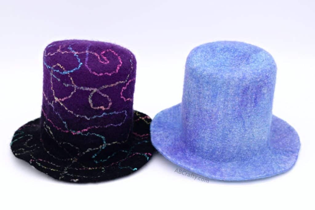 two wet felted top hats. one is black and purple with rainbow swirls and the other is in blue tones