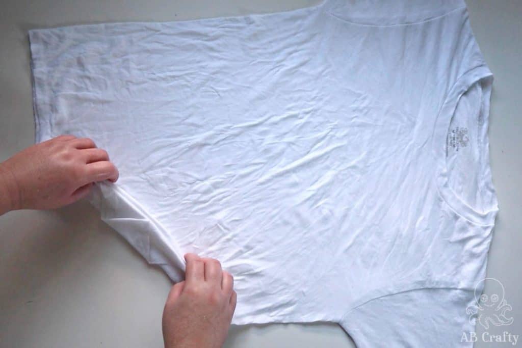 Making multiple diagonal folds in a white t shirt at an angle