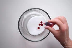 adding drops of red food coloring to white glue in a bowl