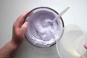 pouring slime activator from a measuring cup into the purple glue and shaving cream mixture
