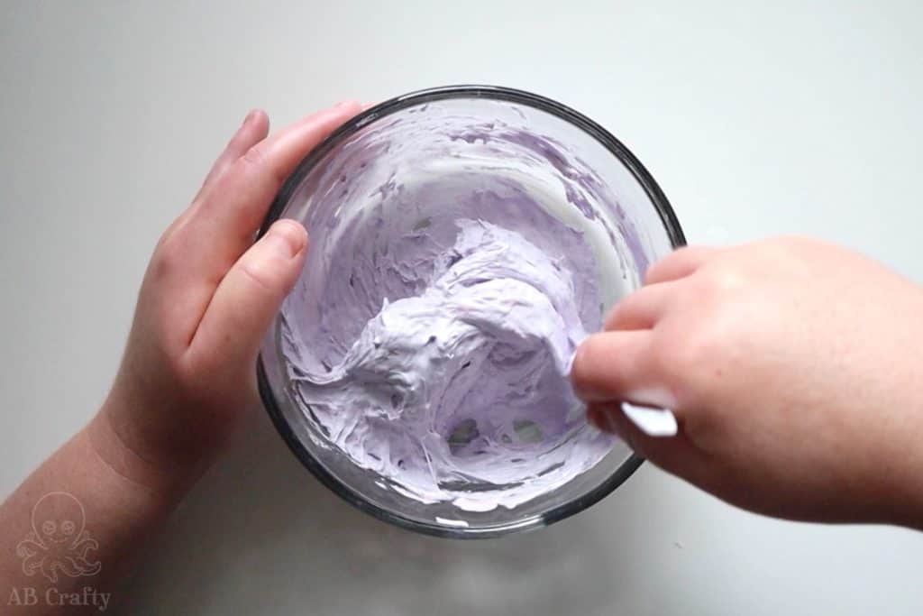 mixing the purple glue and shaving cream mixture with the activator so that it starts to form clumps and detach from the sides of the bowl