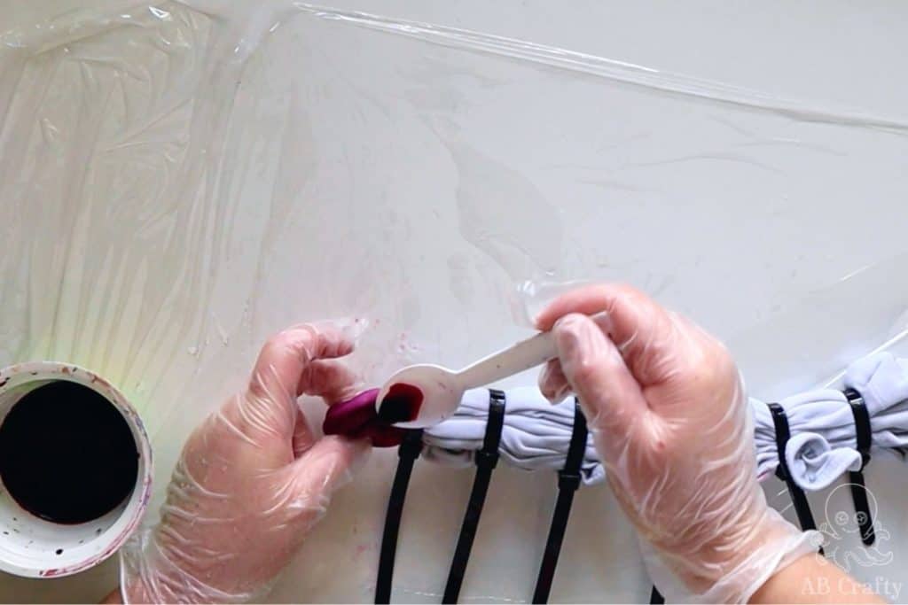 pouring dark pink dye from a spoon onto the first section of the tank top next to the zip tie