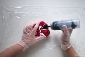 pouring black dye from a squirt bottle onto pink shorts tied with rubber bands