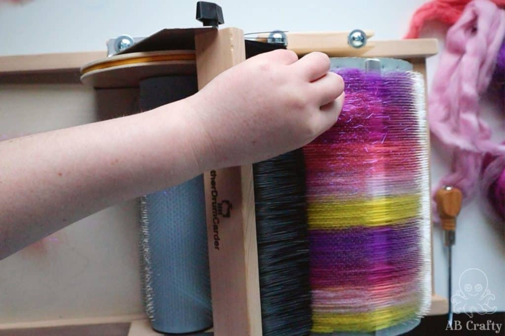 adding pink angelina fiber to the barrel of a carder containing pink, purple, and yellow blended wool