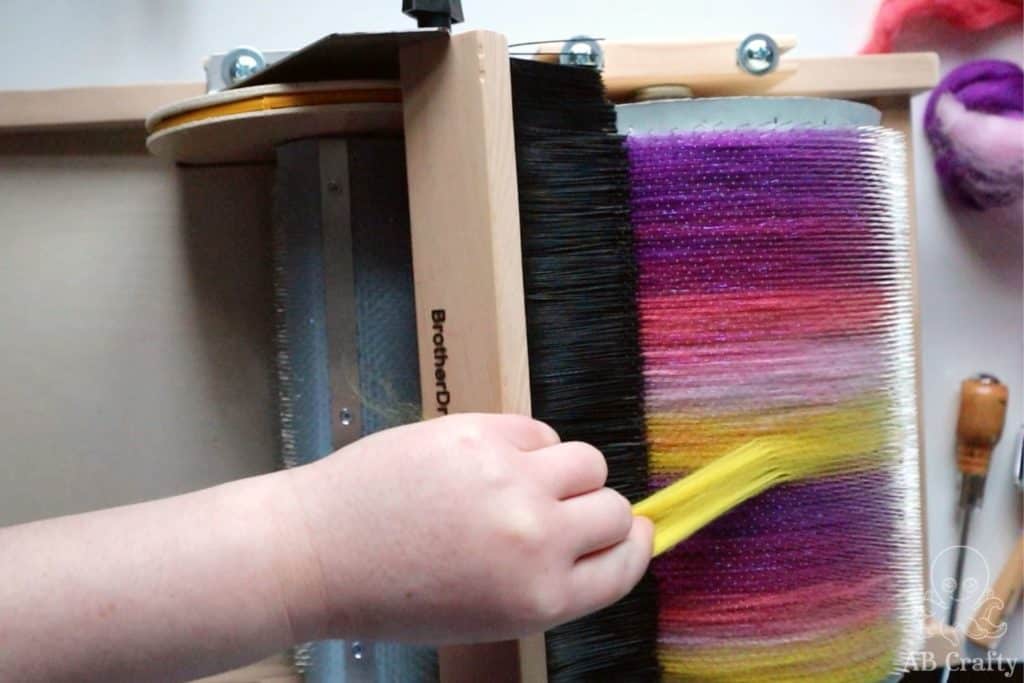 adding yellow wool to the barrel of a carder containing pink, purple, and yellow blended wool