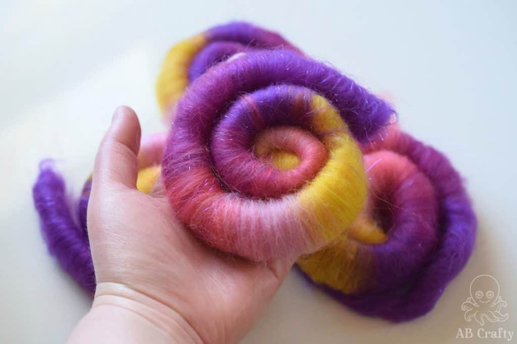 holding a finished pink, purple, and yellow wool rolag