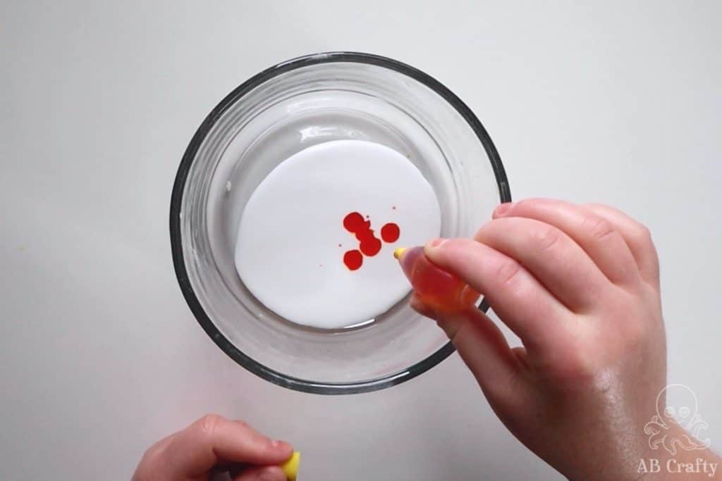 dropping yellow food coloring into white glue in a glass bowl